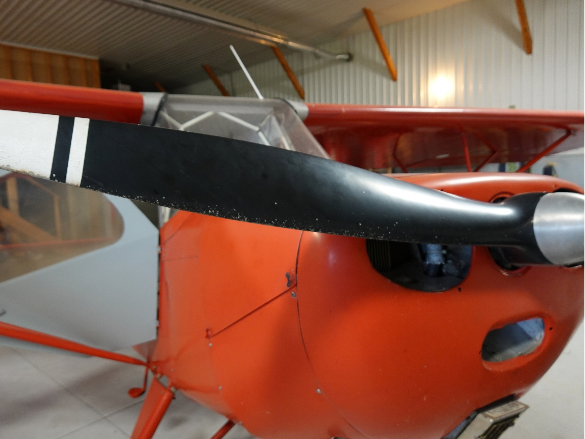 Close up of a red vintage airplane in a hangar showing a black propeller blade and cockpit area