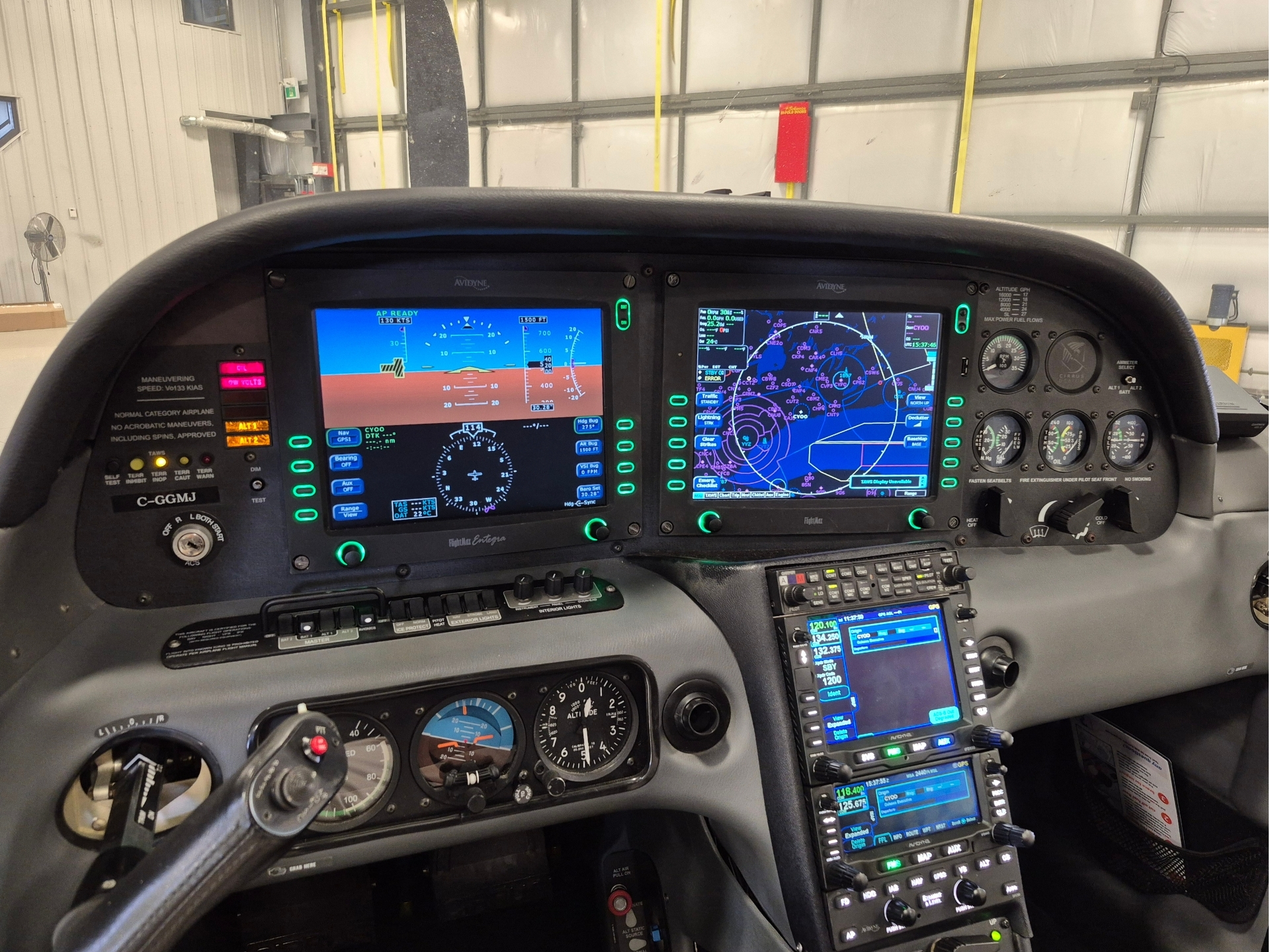Cockpit of a small aircraft with two large glass cockpit displays multiple gauges and a cluttered center console in a hangar body
