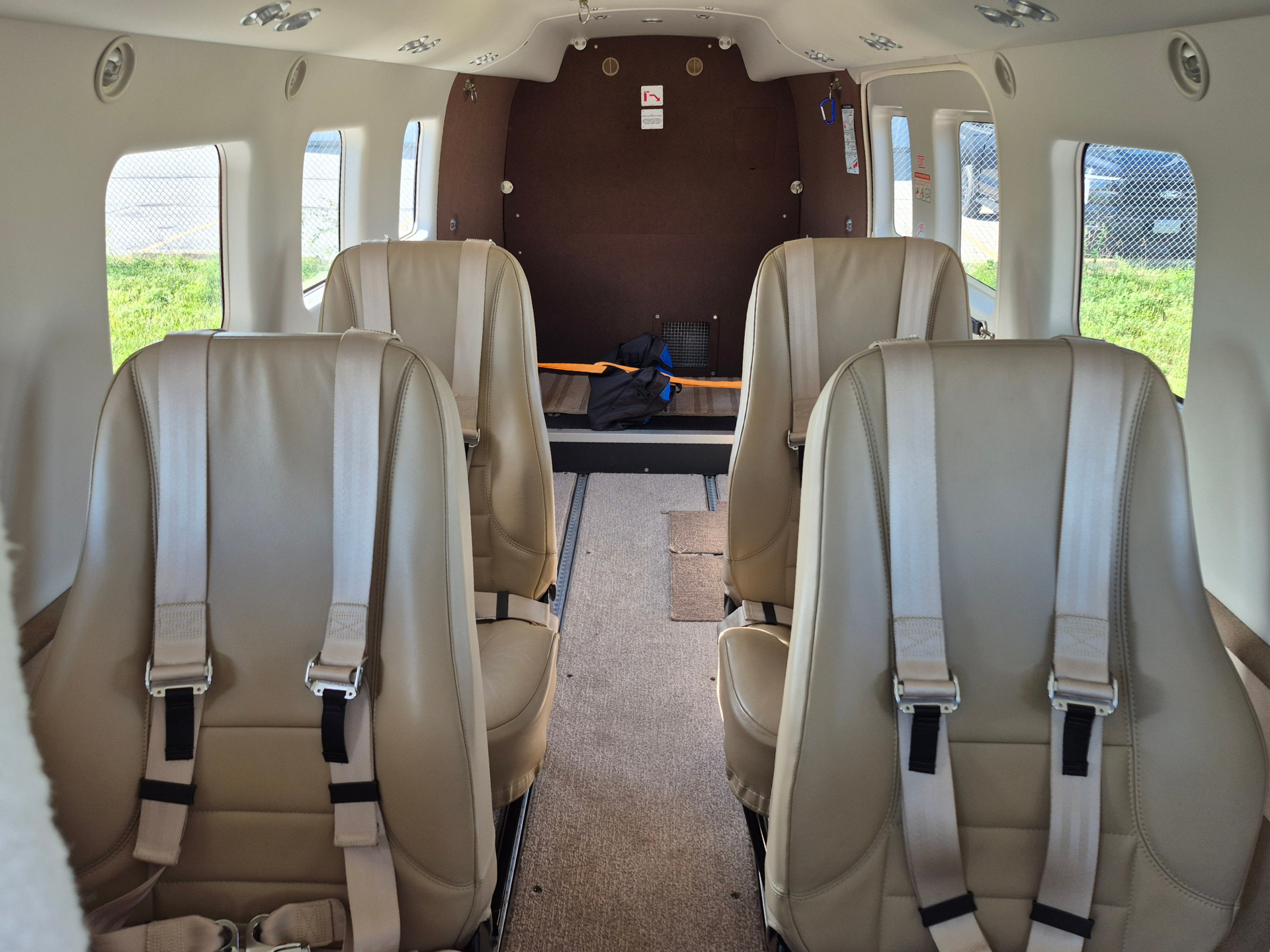 Interior of a small passenger airplane cabin with beige seats and lap belts viewed toward the rear bulkhead and windows along the sides