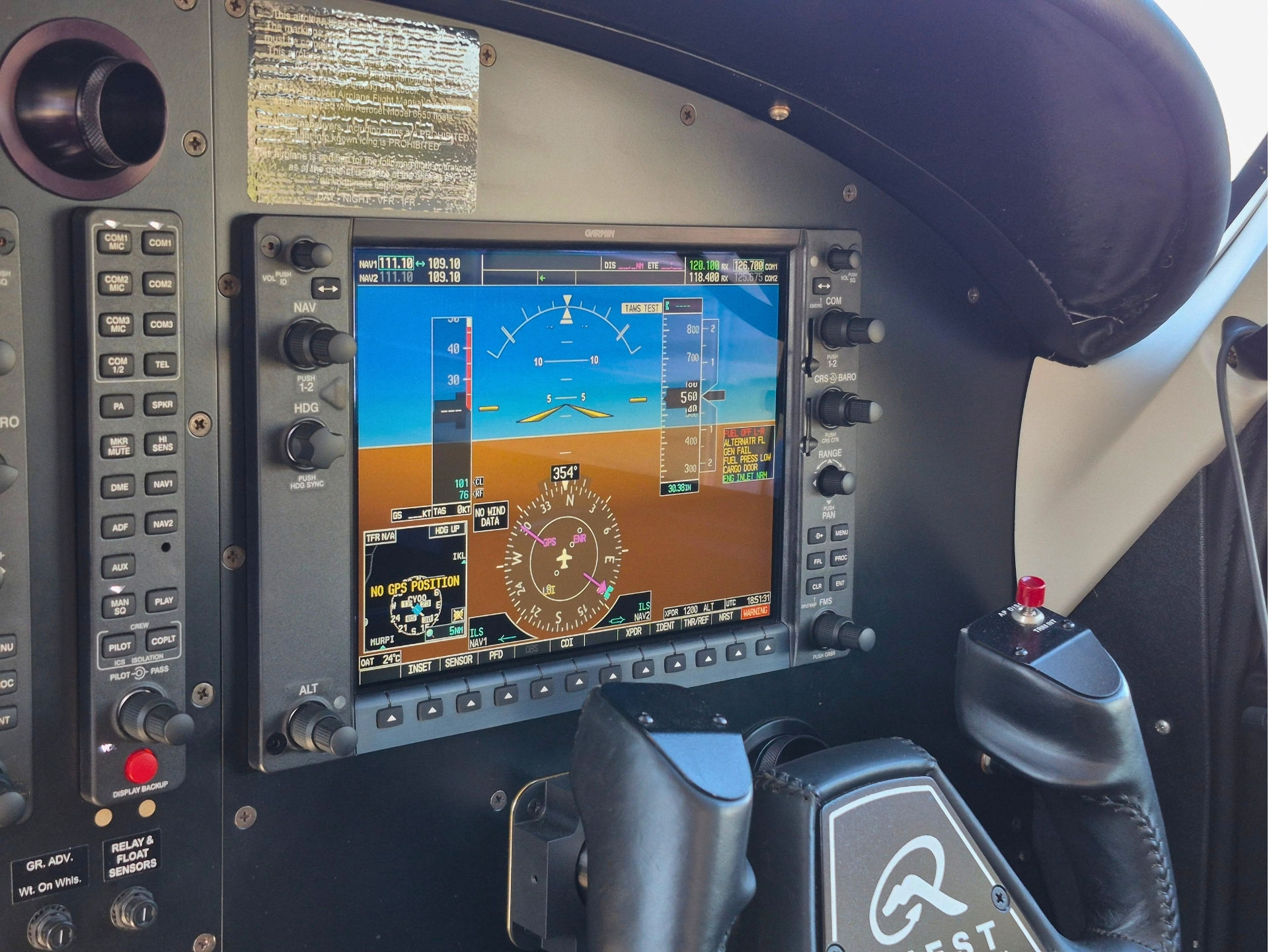 Cockpit of a small aircraft with a Garmin flight display and control panels visible on the left and a yoke in the foreground