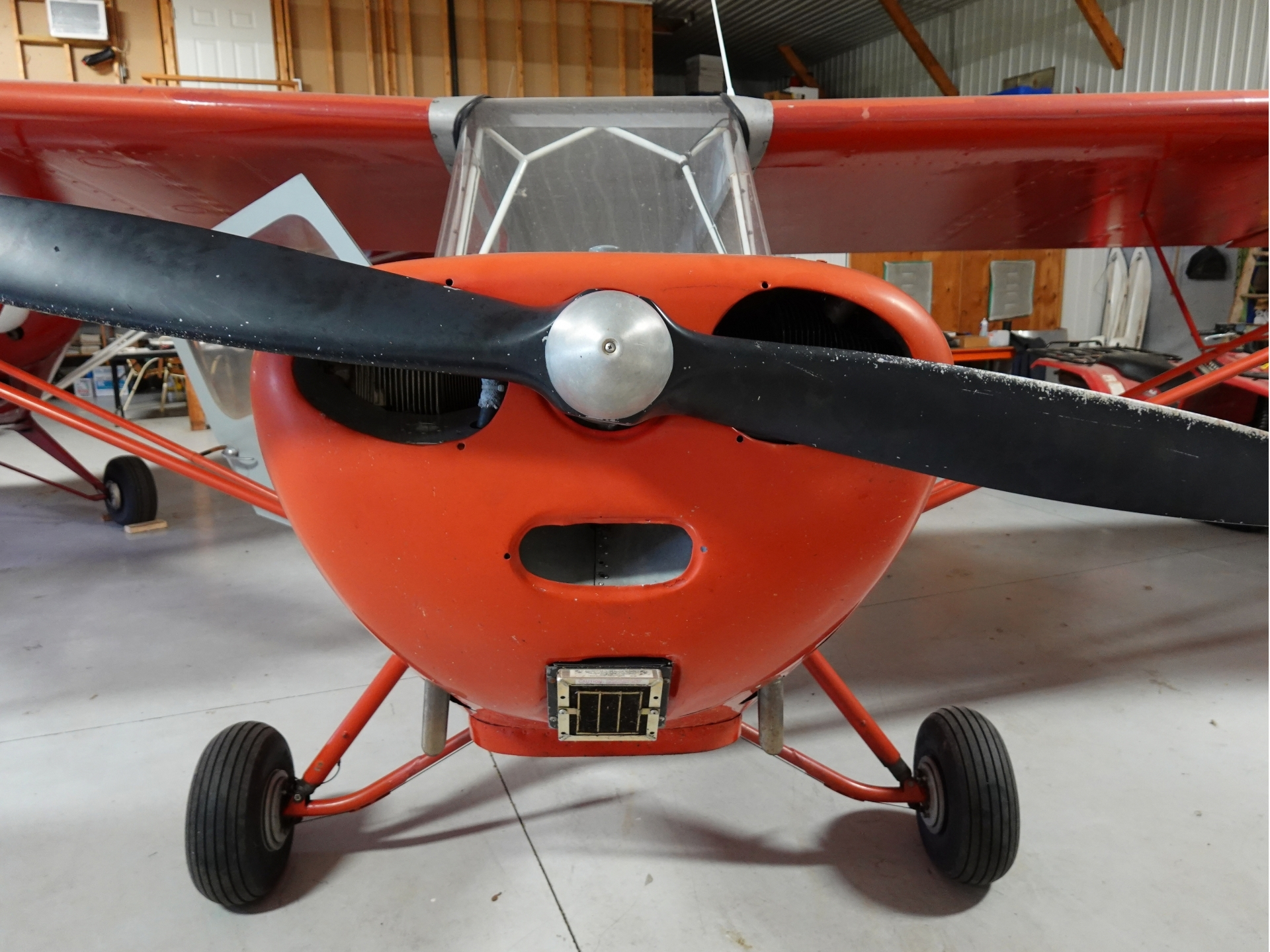 Front view of a red small airplane in a hangar with a black twoblade propeller and clear cockpit canopy