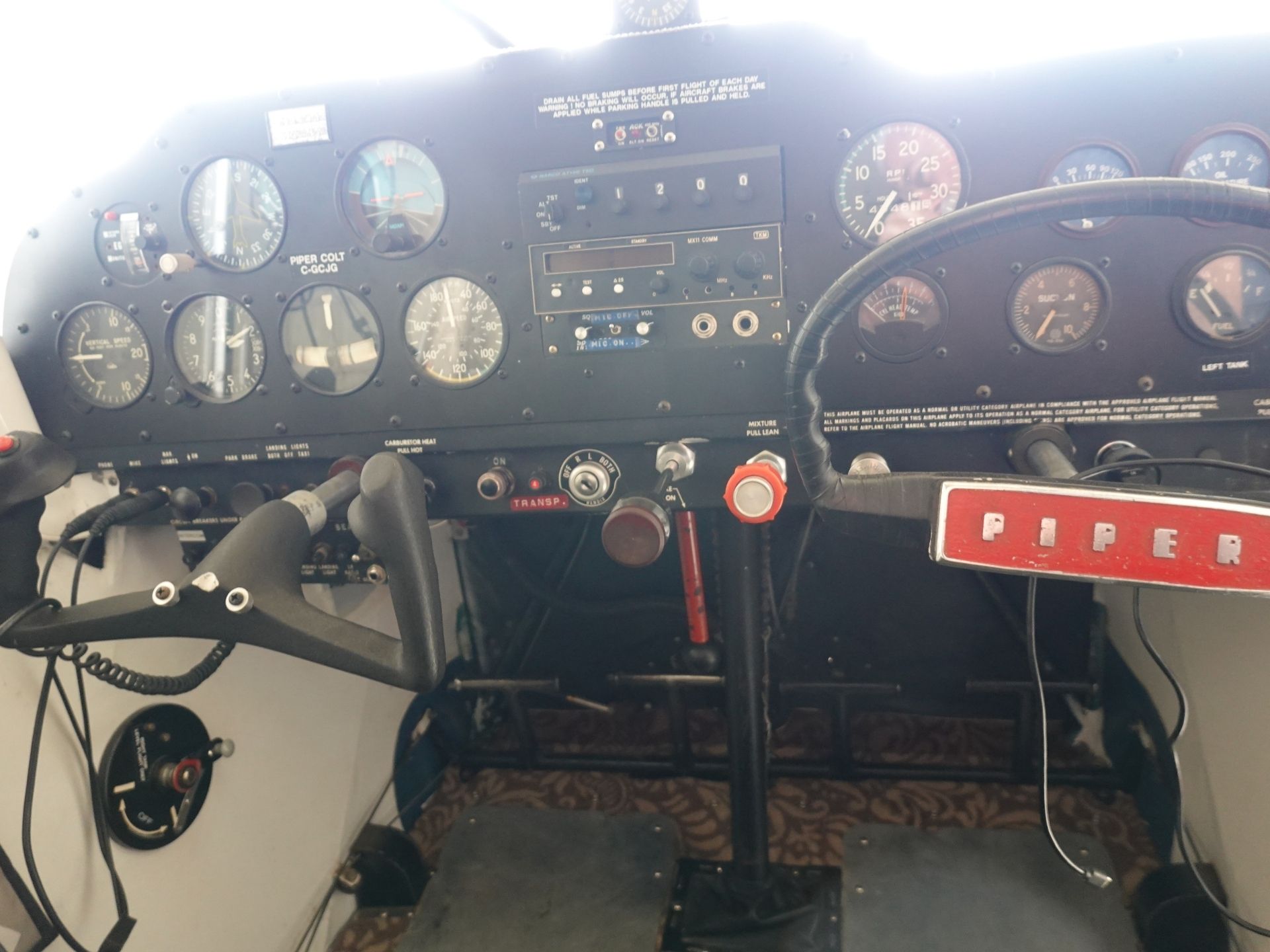 Front cockpit of a small Piper aircraft with numerous analog gauges, a center radio stack, and a dual control yoke.