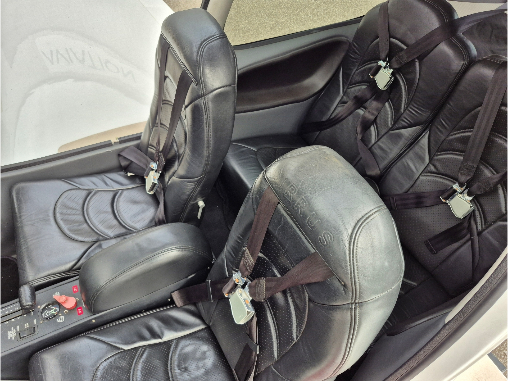 Interior of a small aircraft with black leather seats and shoulder harnesses cockpit controls on the center console