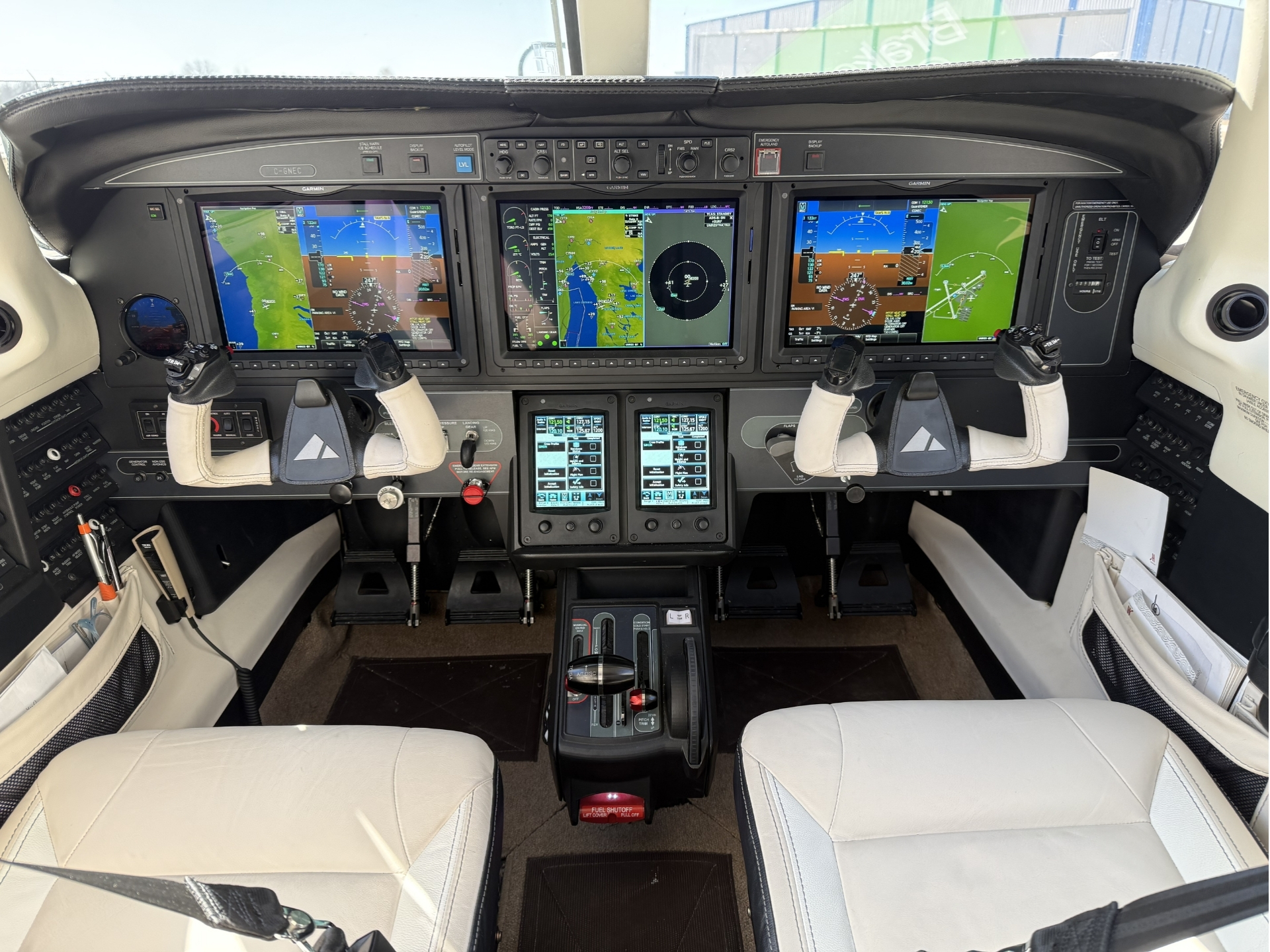 Cockpit of a small aircraft with three large Garmin glass flight displays and dual yokes
